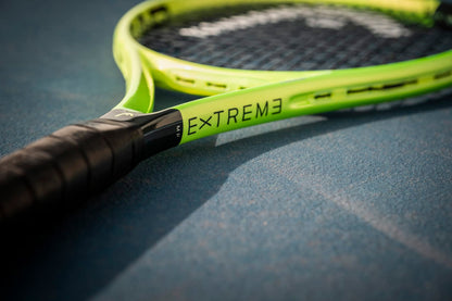 A close-up of the HEAD Extreme MP 2026 Tennis Racket by HEAD, featuring the "EXTREME" label, rests on a blue tennis court and showcases its handle and frame engineered for enhanced power and spin.