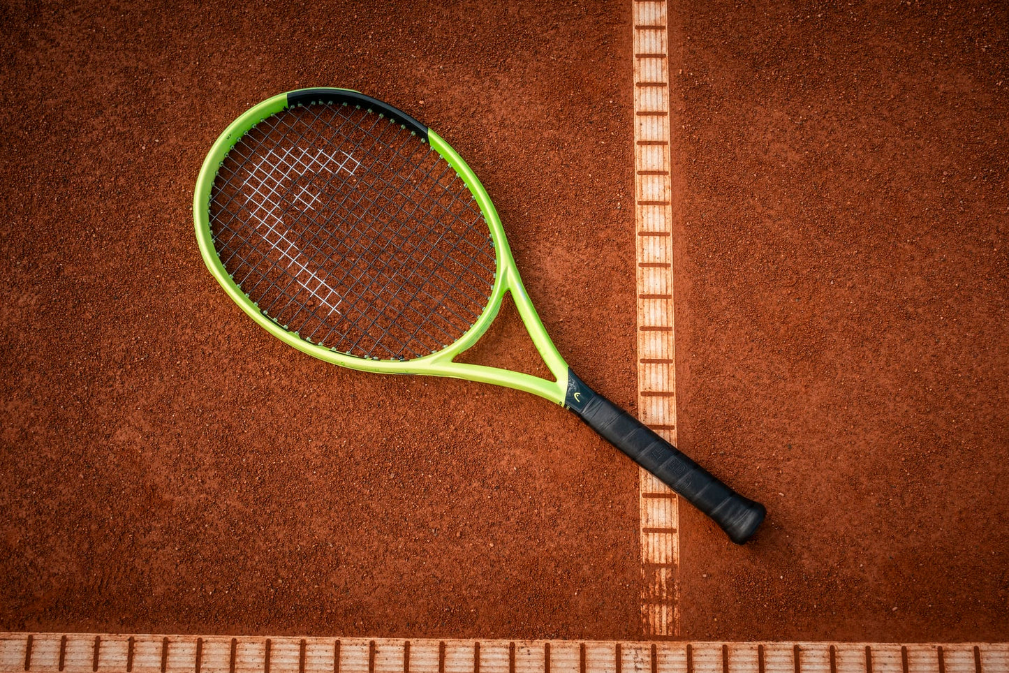A HEAD Extreme MP 2026 Tennis Racket by HEAD, featuring a green and black design, rests on a clay court with its frame partially over a crisp white boundary line—poised to unleash impressive spin and power with each swing.
