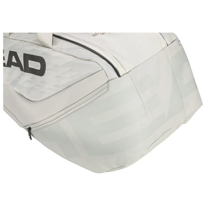 The image shows a detailed view of an off-white and light gray tennis racket bag with a zippered compartment, featuring the HEAD Pro X Tennis Racket Bag - M - YUBK logo in gray, inspired by Novak Djokovic's renowned SPEED racquet series.