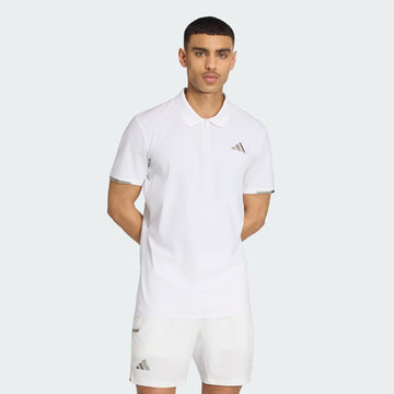 A man stands with his hands behind his back against a light gray background, wearing an adidas Climacool Mens Tennis Polo Shirt in white and matching shorts, both featuring the adidas logo.