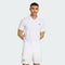 A man stands with his hands behind his back against a light gray background, wearing an adidas Climacool Mens Tennis Polo Shirt in white and matching shorts, both featuring the adidas logo.