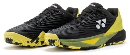 A pair of Yonex Power Cushion Eclipsion 5 Men’s Tennis Shoes in black and yellow, featuring the Yonex logo in white, black laces, and patterned yellow soles, are placed side by side on a white background.