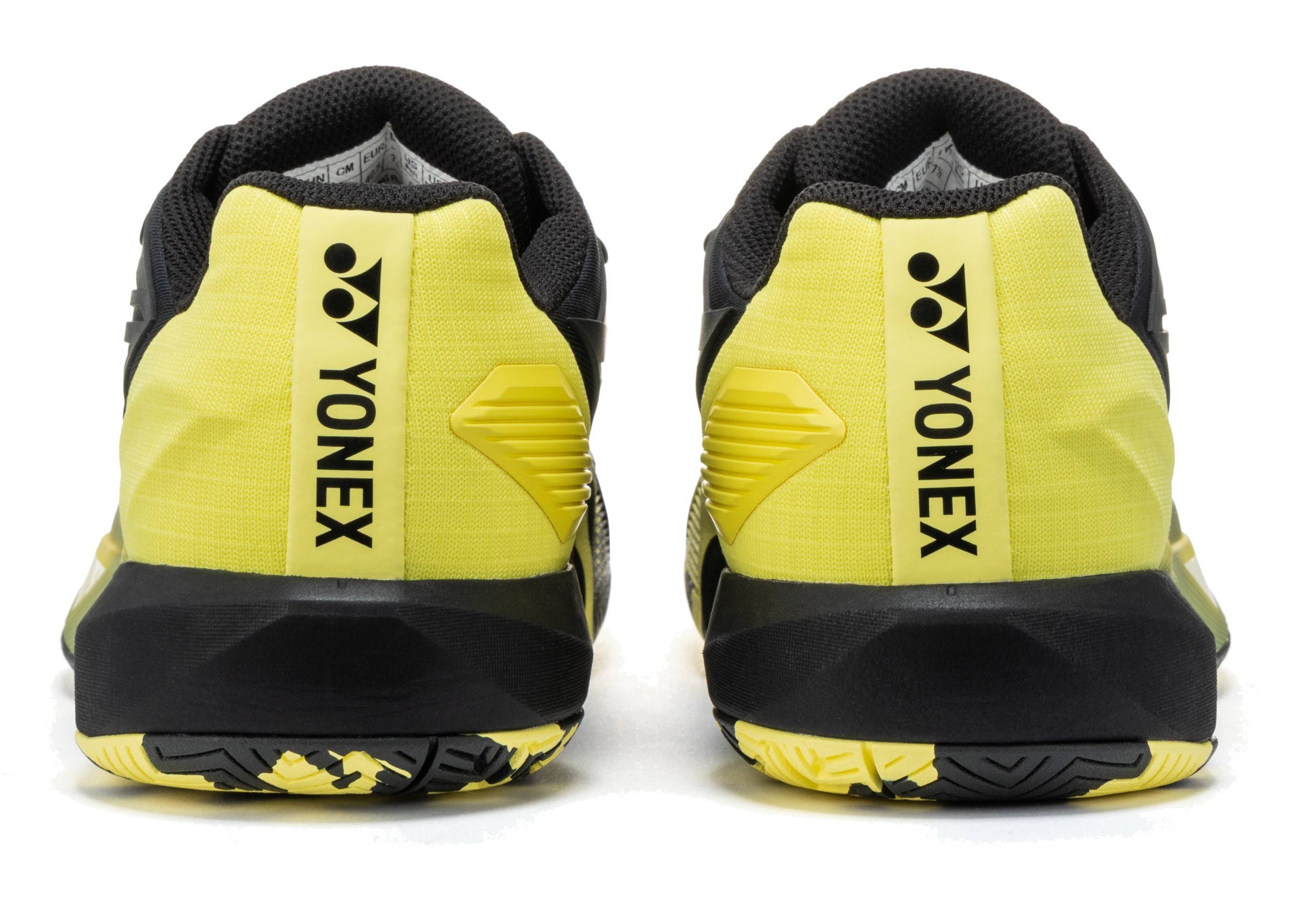 Here’s a rewritten version using the given product data: The Yonex Power Cushion Eclipsion 5 Men’s Tennis Shoes in black and yellow are shown from the back, displaying the Yonex logo and name printed vertically on the heel. These men’s tennis shoes feature Yonex Power Cushion technology to provide enhanced comfort and stability on the court.