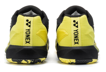 Here’s a rewritten version using the given product data: The Yonex Power Cushion Eclipsion 5 Men’s Tennis Shoes in black and yellow are shown from the back, displaying the Yonex logo and name printed vertically on the heel. These men’s tennis shoes feature Yonex Power Cushion technology to provide enhanced comfort and stability on the court.