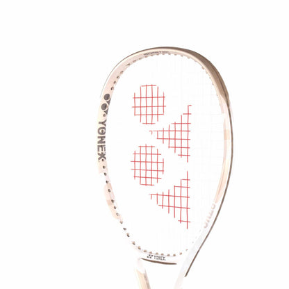 A close-up of the Yonex VCORE Feel Tennis Racket in Sand Beige emphasizes its unique string pattern with red graphics. The frame shines in white and gold, featuring the logo on the side. With ISOMETRIC technology, it ensures precision against a plain white background.
