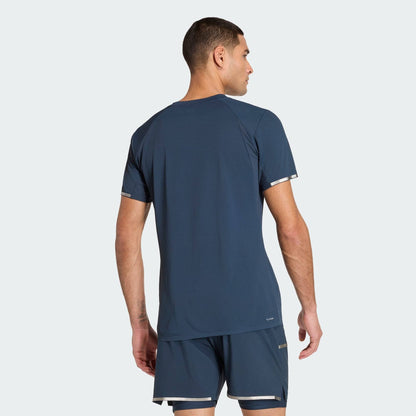 A man wearing the adidas Climacool+ Freelift Pro Mens Tennis T-Shirt - Aurora Ink stands with his back to the camera against a plain light gray background.