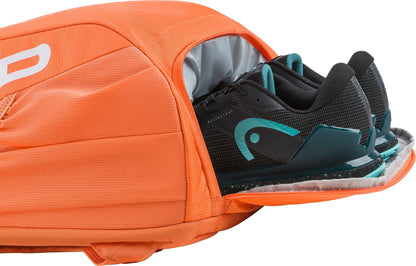 A pair of black and teal athletic shoes are partially packed in an open zipper compartment of the HEAD Tour 25L Tennis Backpack - Orange by HEAD.