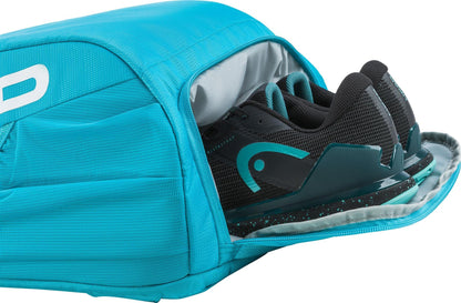 A pair of black and teal athletic shoes are partially packed inside an open, bright blue HEAD Tour 25L Tennis Backpack by HEAD with side pockets.