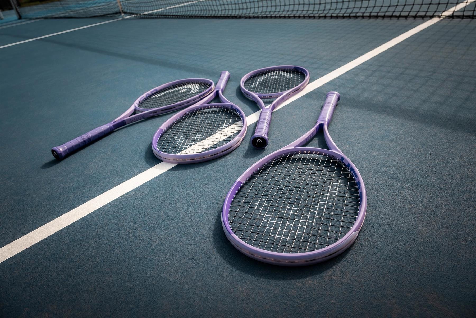 Four HEAD Boom MP UL Alternate 2026 Tennis Rackets from HEAD lay on a blue court near the white boundary line, with the net visible in the background.