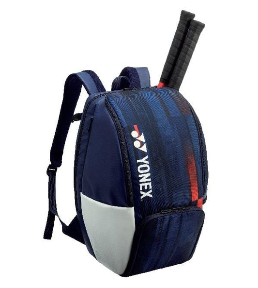 The Yonex BA12PAEX LTD Pro Tennis Backpack in white, navy, and red is crafted from eco-friendly materials. It features two shoulder straps and prominently displays the Yonex logo. The design allows for two tennis rackets to be partially tucked into the top compartment for easy access.