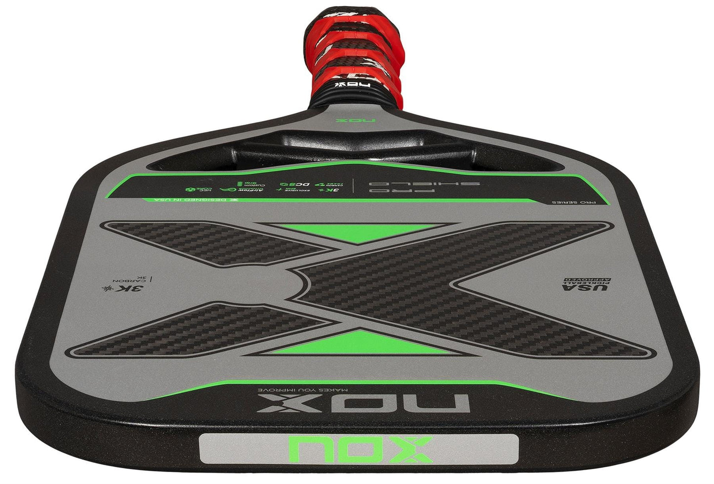 A close-up of the NOX NOV Pro Shield Pickleball Paddle in black and green, featuring Spin Technology, a red and black handle, and bold "NOX" branding on the carbon fibre face.