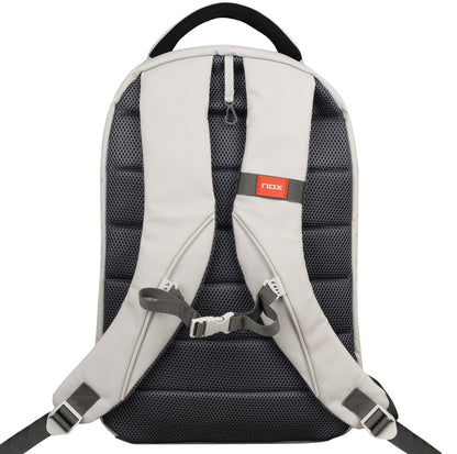 A cream NOX Pro Pickleball Backpack by NOX is shown from the back, featuring ergonomic padded straps with ThermoTech technology, a sternum strap, carrying handle, and a small red label on the upper right strap.