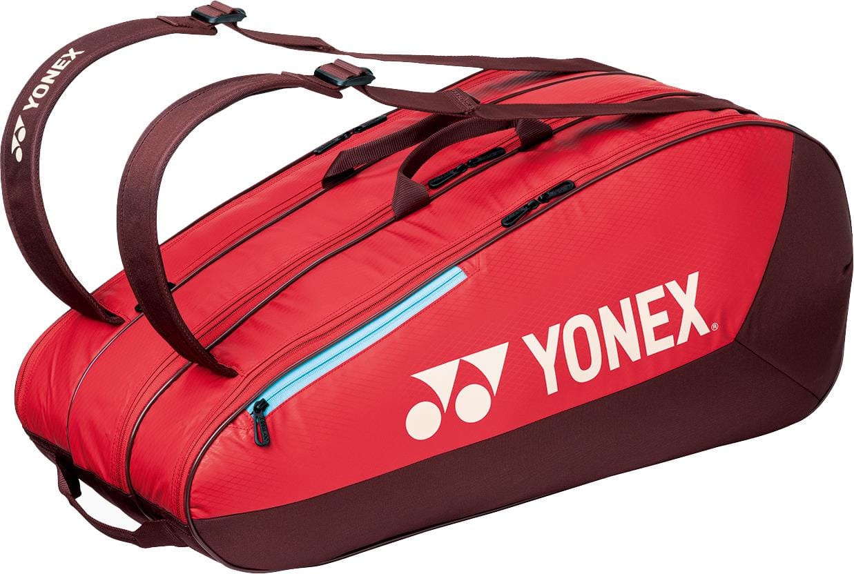 The Yonex 42529EX Team 9 Racket Tennis Bag in ruby red features black zippers, blue accents, and two dark brown straps. The white Yonex logo stands out on the side—ideal for carrying your tennis gear in style.