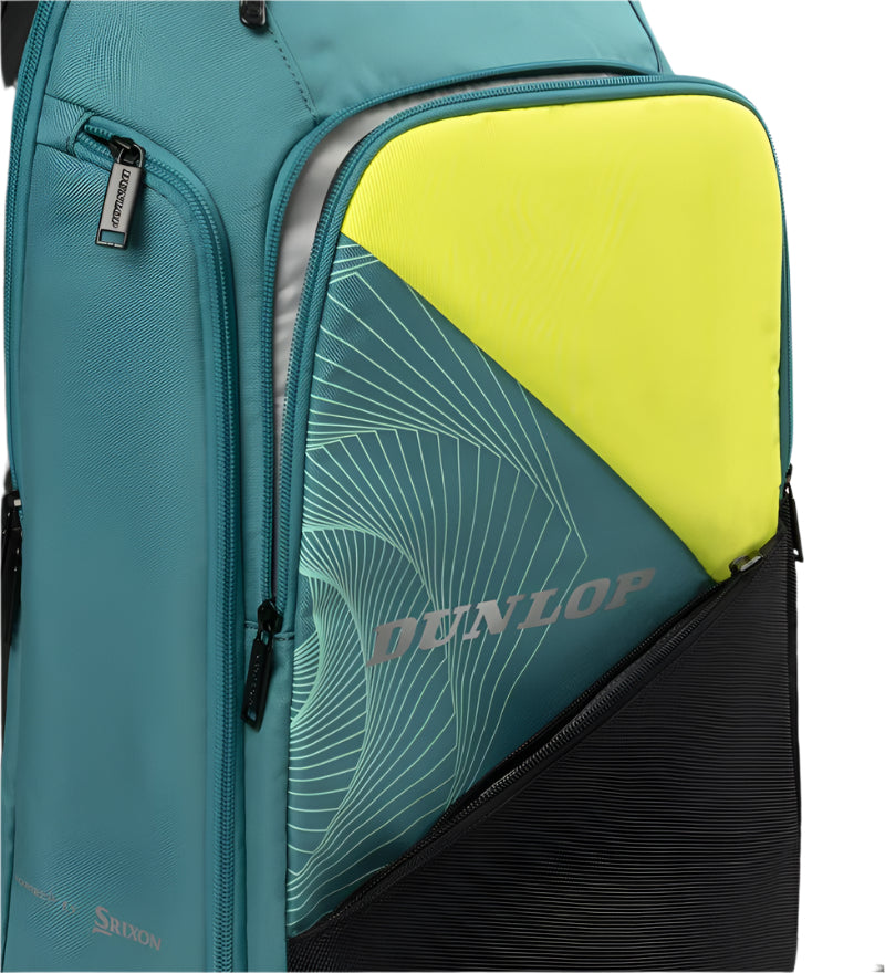 The Dunlop SX Performance Tennis Backpack in teal, black, and yellow is partially open, showing a yellow folder with a geometric pattern and "Dunlop" logo. It features ergonomic shoulder straps, multiple zippered compartments with black detailing, and has dedicated racket storage.