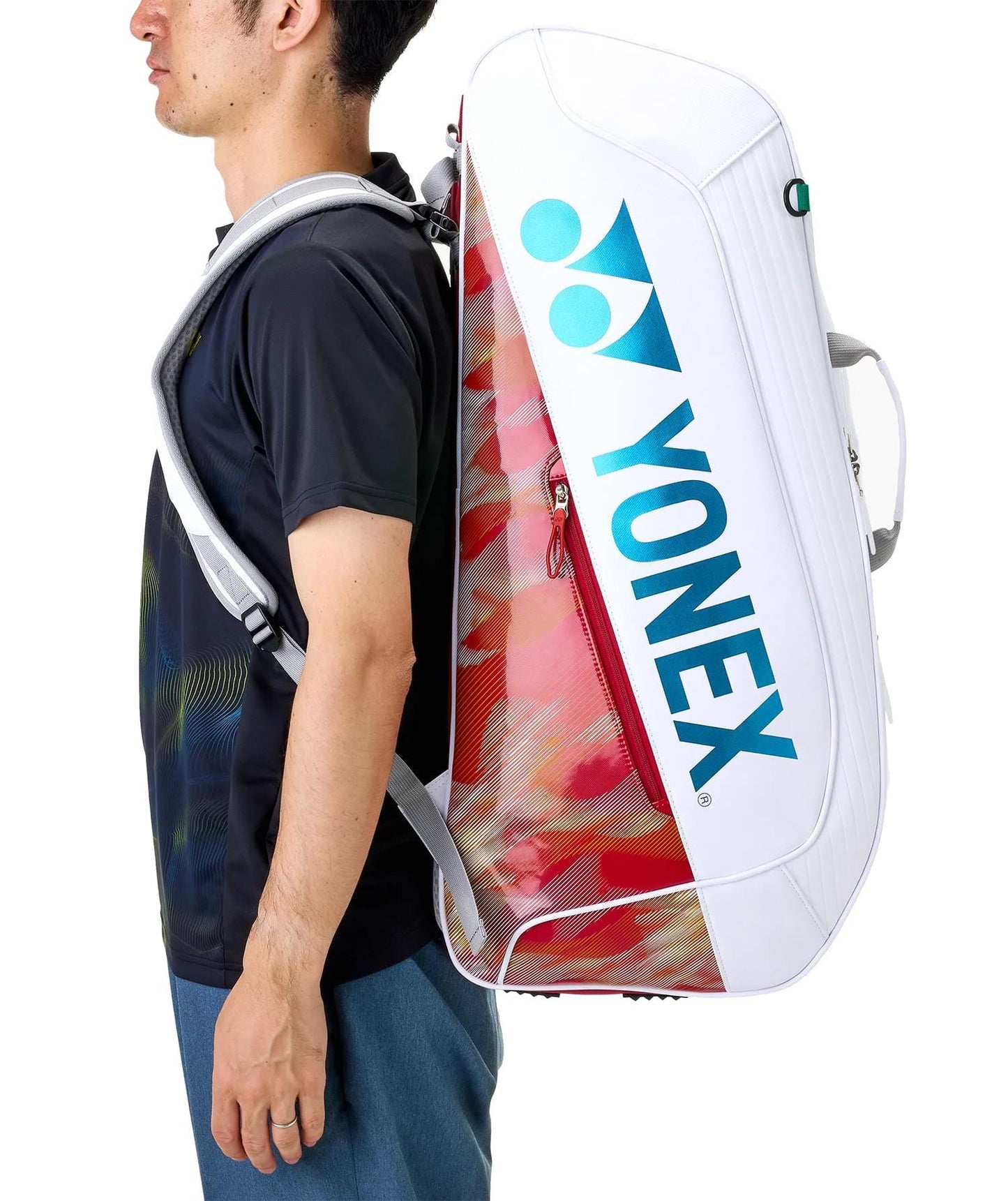 A person stands sideways to the camera with a Yonex 02626EX Expert 6 Racket Tennis Bag - White slung across their back, featuring blue lettering and racket thermoguard.