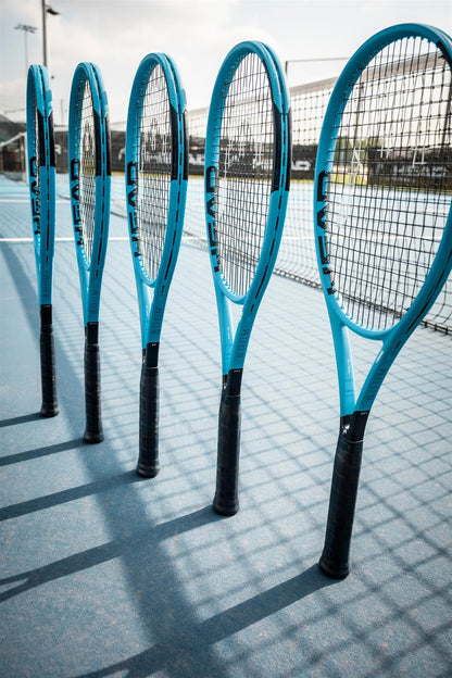 Five HEAD Boom Team 2026 Tennis Rackets stand upright on a blue court, their black handles casting shadows. A net and fencing appear in the background.