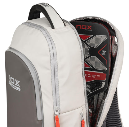 A cream NOX Pro Pickleball Backpack is partially unzipped, showing a black and red NOX paddle racket in its padded compartment; the backpack features ergonomic padded straps for comfort.