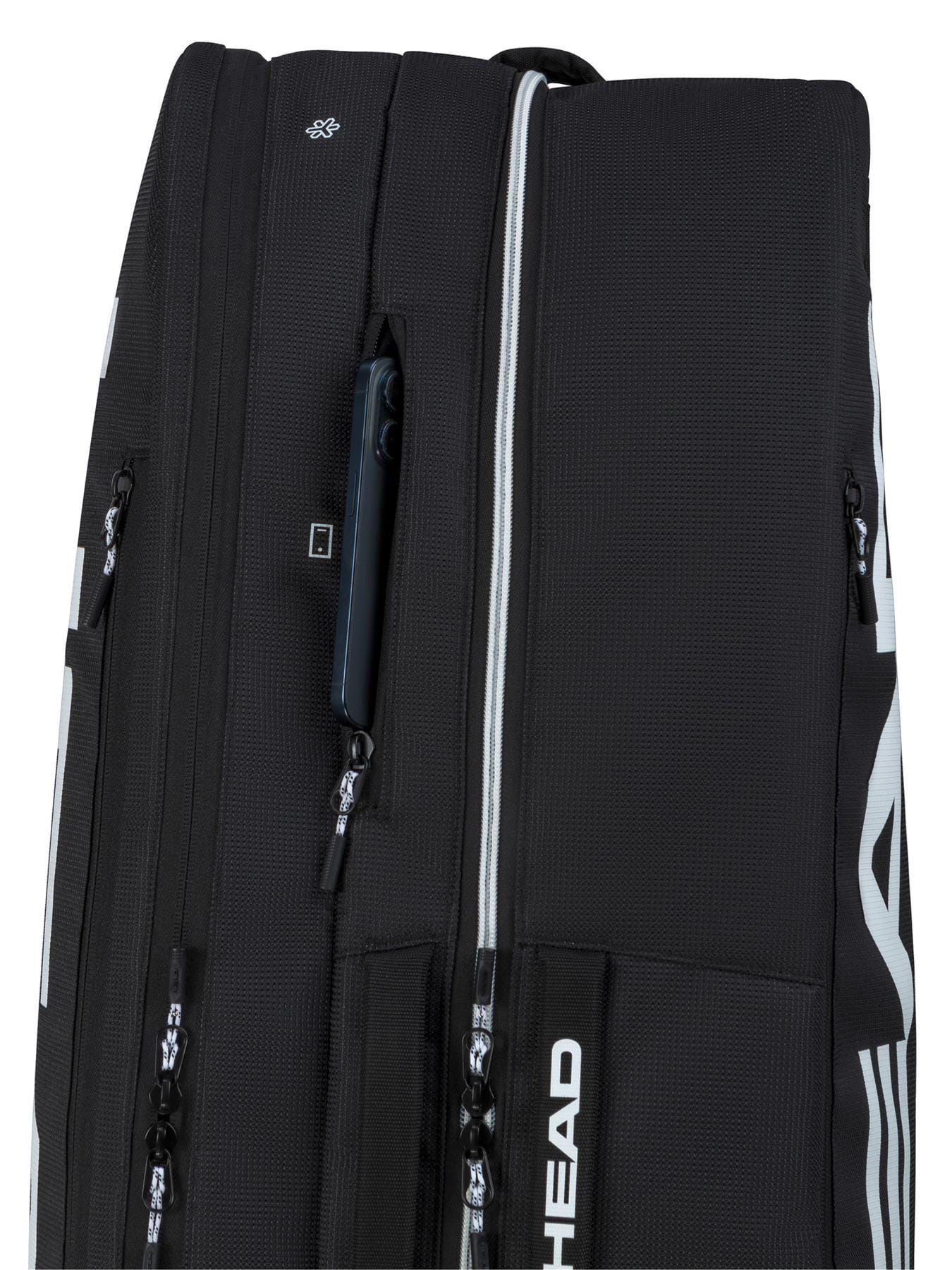 Close-up of the HEAD Tour 9 Racket Tennis Bag L in black, showing multiple zippered compartments and a smartphone in one pocket. The brand name "HEAD" is printed vertically in white on the bag.