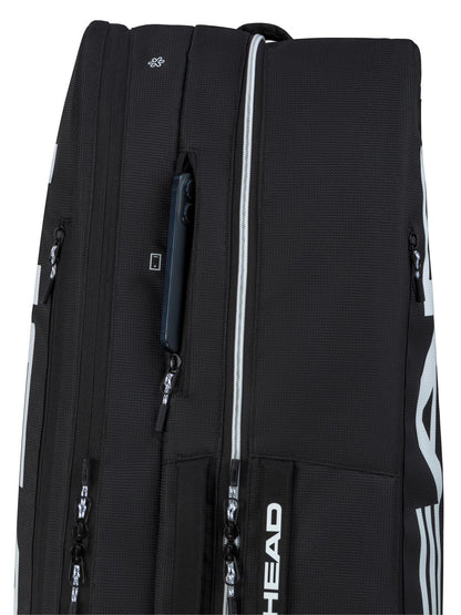 Close-up of the HEAD Tour 9 Racket Tennis Bag L in black, showing multiple zippered compartments and a smartphone in one pocket. The brand name "HEAD" is printed vertically in white on the bag.