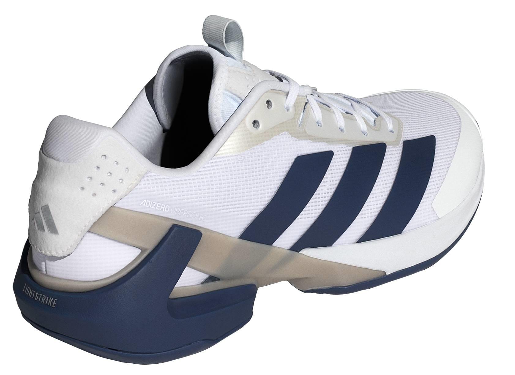 The adidas Adizero Ubersonic 5 Men’s Tennis Shoes in White/Navy feature a mesh and synthetic upper, modern design, and chunky angular navy sole—delivering lightweight comfort inspired by the iconic ADIDAS Ubersonic 5.