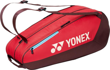 The Yonex 42526EX Team 6 Racket Tennis Bag in Ruby Red features two shoulder straps, a blue zipper pocket, and a white Yonex logo on the side. Ideal for carrying up to 6 rackets for all your tennis needs.