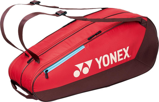 The Yonex 42526EX Team 6 Racket Tennis Bag in Ruby Red features two shoulder straps, a blue zipper pocket, and a white Yonex logo on the side. Ideal for carrying up to 6 rackets for all your tennis needs.