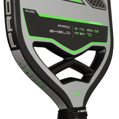 Close-up of the NOX NOV Pro Shield Pickleball Paddle in black and green, showcasing technical specs, advanced Spin Technology on its carbon fibre face, and part of the NOX logo on the handle.