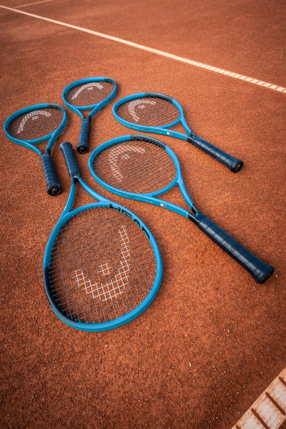 Four HEAD Boom Pro 2026 Tennis Rackets by HEAD, in blue, are placed overlapping on a clay court near the white sideline—ideal for advanced players looking for explosive power.