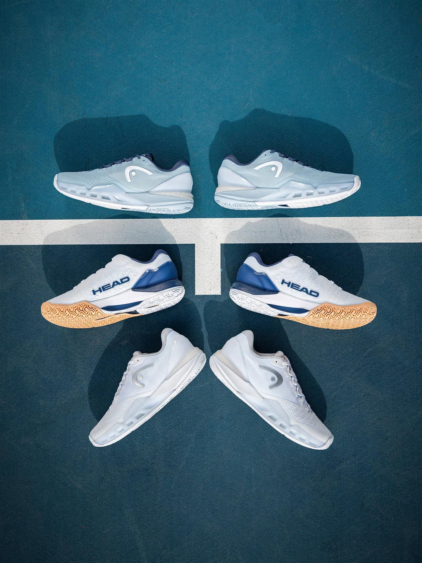 Three pairs of women's tennis shoes are arranged vertically on a blue court, with the HEAD Revolt Pro 5.0 Womens Tennis Shoes - White / Apricot by HEAD featured in the center over a white court line.