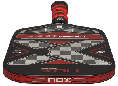 A close-up of the NOX Luxury Nerbo Pickleball Paddle by NOX, in black and red, highlighting its large “X” design, detailed graphics, aluminised carbon fibre surface, and textured grip handle.