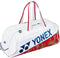 The Yonex 02631WEX Expert Tournament Tennis Bag in white features red handles, blue Yonex logo and name, a subtle red and gold pattern on the bottom edge, plus Thermo Guard technology to protect your gear at tournaments.