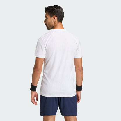 A man faces away from the camera, wearing an adidas Climacool+ Airchill Freelift Men's Tennis T-Shirt in white, navy shorts, and black wristbands, set against a plain light gray background.