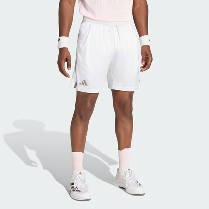 A person stands against a plain light background wearing adidas Climacool Ergo Pro Mens Tennis Shorts in white, paired with a light pink shirt, white wristbands, pink socks, and white sneakers. Their head is not visible in the image.