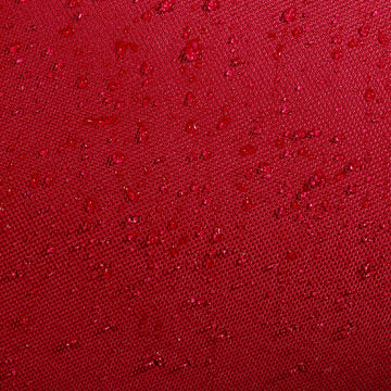 Close-up of burgundy water-resistant fabric on the Babolat Court XS 3 Racket Tennis Bag - Burgundy / Black, with scattered water droplets beading on the surface, highlighting the compact Babolat bag's waterproof texture.