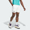 A person in a teal shirt, adidas Climacool Ergo Mens Tennis Shorts (white), white adidas socks, and white sneakers with purple and yellow accents stands against a plain light background.