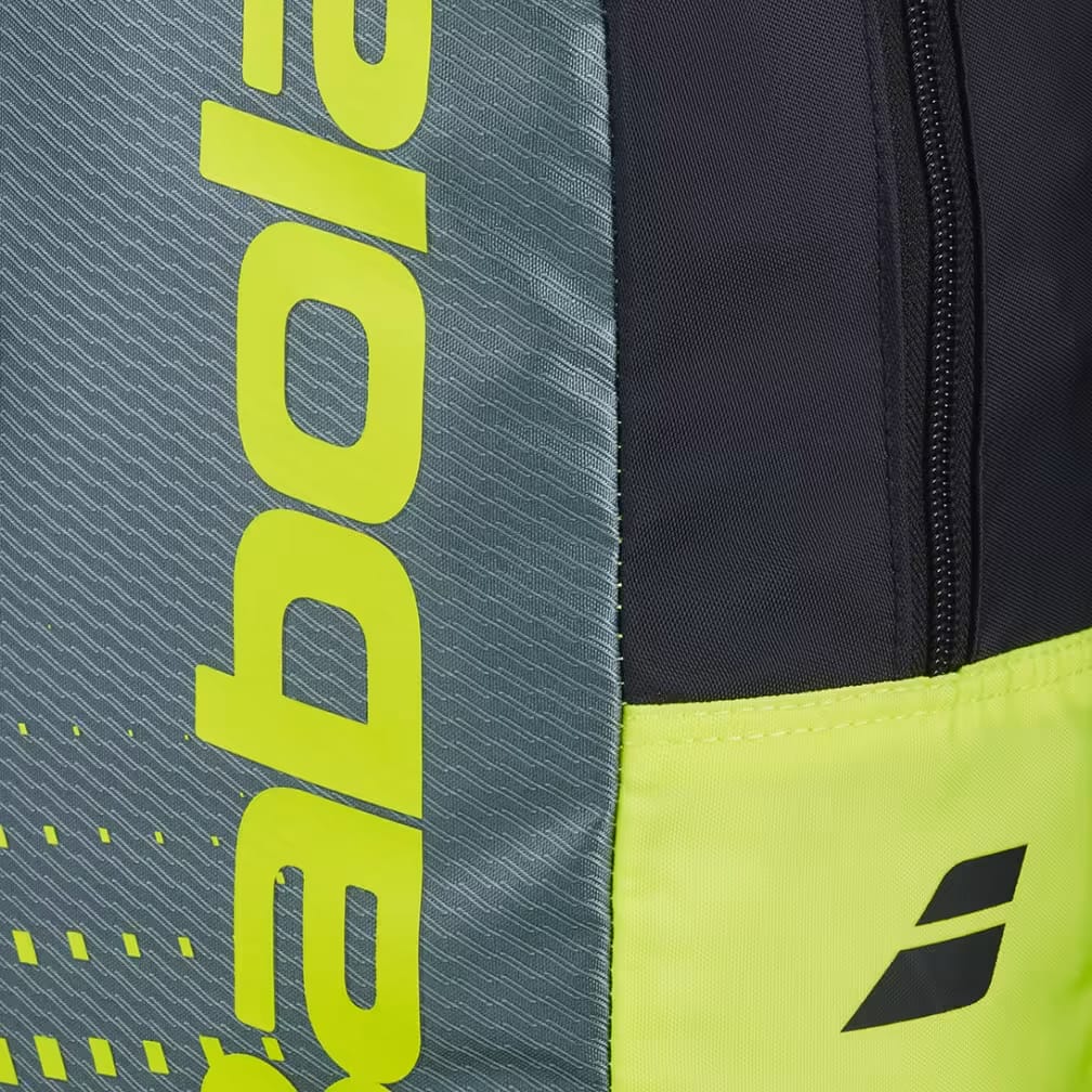 Close-up of the Babolat Kids Tennis Backpack - Metallic Grey / Fluo Yellow, showcasing a gray side panel with bold, bright yellow vertical "Babolat" text and a vibrant fluo yellow bottom section featuring a small black Babolat logo. These sections are divided by a black fabric strip with a zipper. Designed for young players, this Babolat kids tennis backpack combines style and functionality, making it an ideal tennis bag for children.