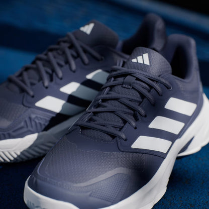 Close-up of adidas CourtJam Control 3 Men’s Tennis Shoes in Dark Blue and Cloud White, featuring signature white stripes and white soles, displayed on a blue textured surface for enhanced stability.