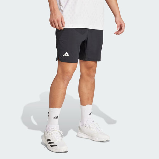 A person wearing adidas Climacool Ergo Men's Tennis Shorts in black, with white adidas crew socks and sneakers, stands against a plain light background. Only the lower body and part of the torso are visible. The shorts are sweat-wicking.