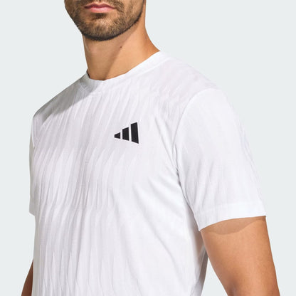 A man wears the adidas Climacool+ Airchill Freelift Men's Tennis T-Shirt in white, featuring a black adidas logo on the left chest, subtle textured pattern, and advanced cooling technology. Only his upper body is shown.