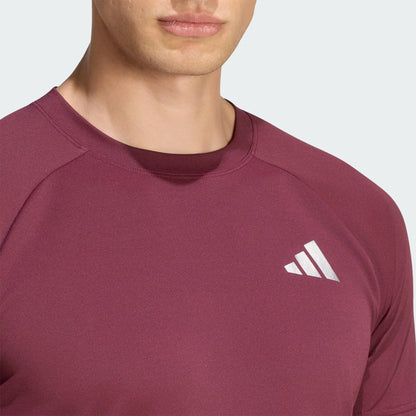 A close-up of a person wearing the adidas Climacool+ Freelift Pro Men’s Tennis T-Shirt in maroon, featuring a white adidas logo on the chest. Only the lower half of the face and upper torso are visible.