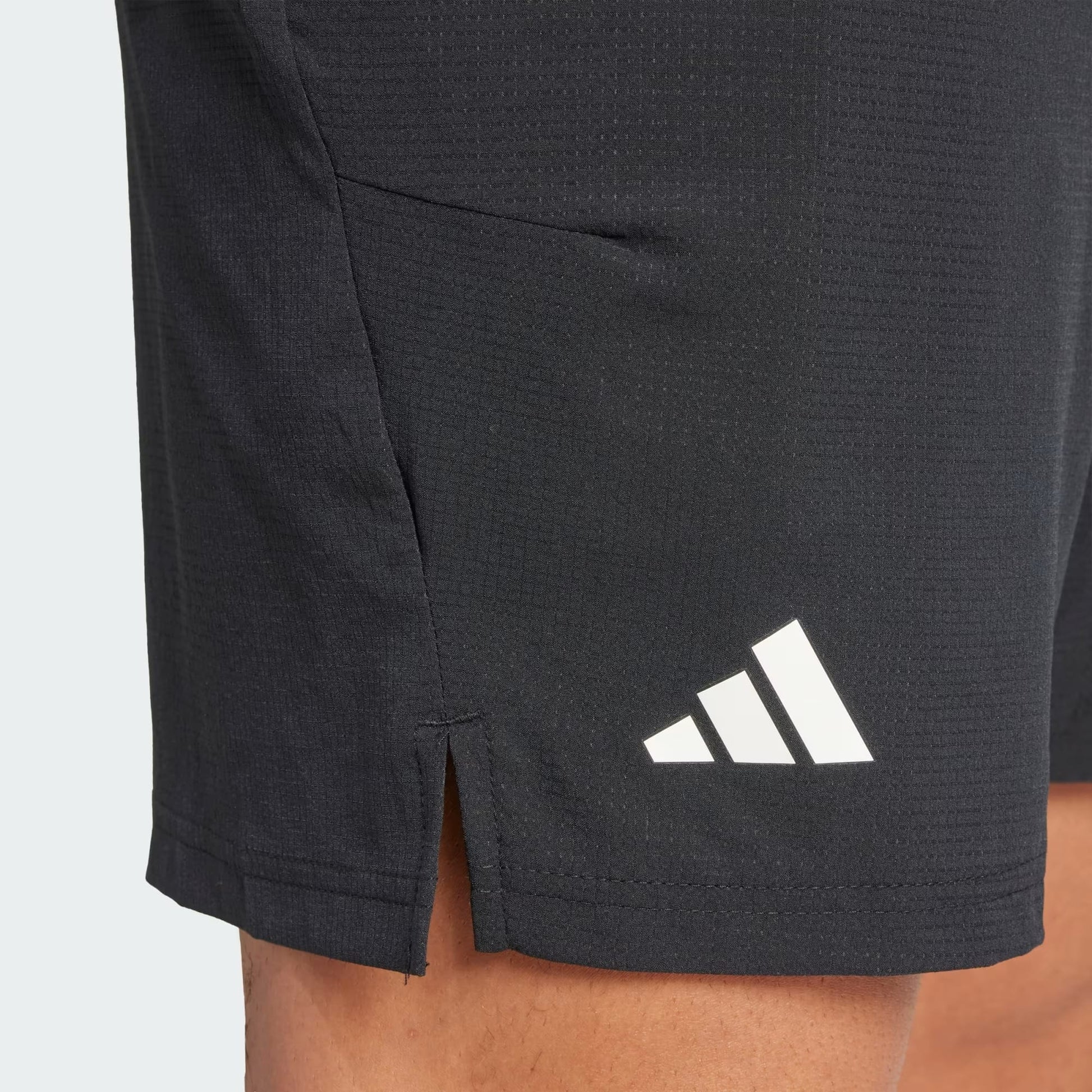 Close-up of a person wearing adidas Climacool Ergo Mens Tennis Shorts in black, featuring the white adidas logo on the lower left leg, a side slit near the hem, and sweat-wicking fabric for comfortable tennis play.