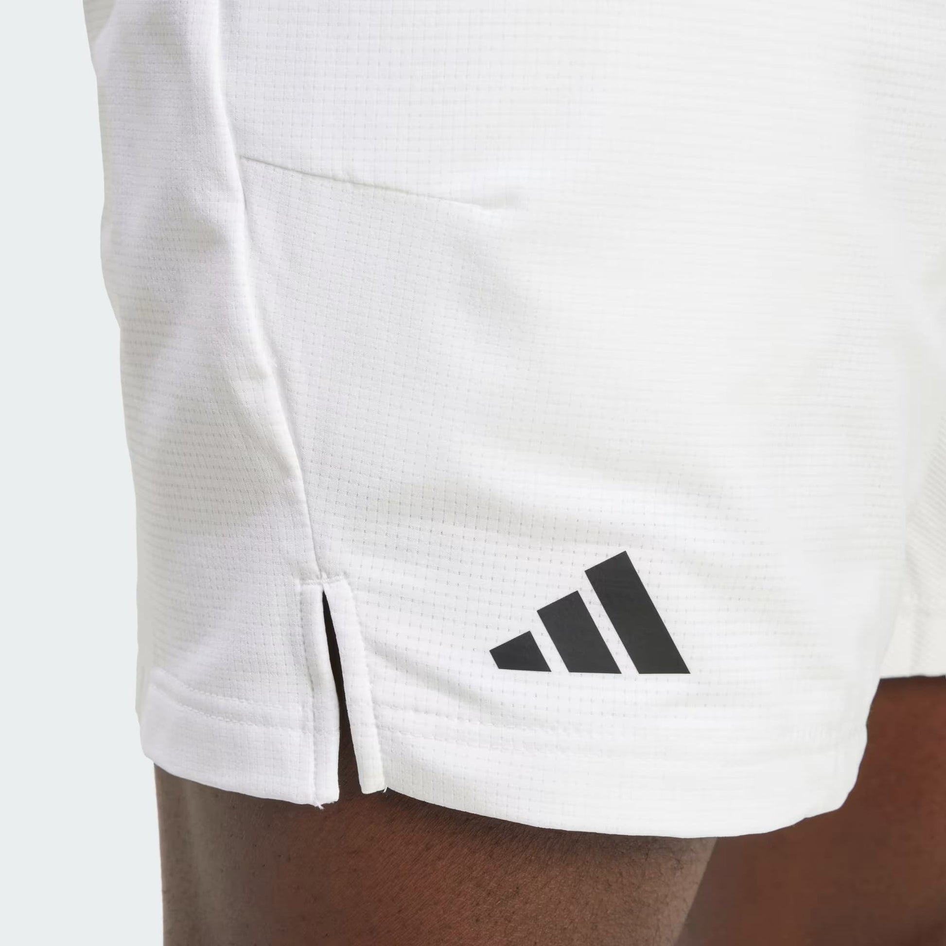 Close-up of a person wearing adidas Climacool Ergo Mens Tennis Shorts - White, featuring a black adidas logo on the left leg, textured four-way stretch fabric, and small side slit hems for comfort.