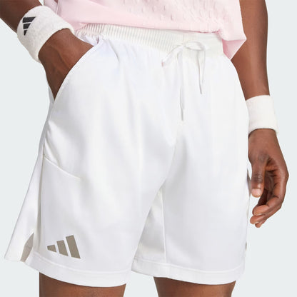 A person is shown from the waist to mid-thigh against a light background, wearing adidas Climacool Ergo Pro Men’s Tennis Shorts in white and adidas wristbands, with hands in pockets.
