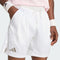 A person is shown from the waist to mid-thigh against a light background, wearing adidas Climacool Ergo Pro Men’s Tennis Shorts in white and adidas wristbands, with hands in pockets.