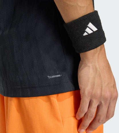 A close-up of a person's arm in the adidas Climacool+ Airchill Freelift Men's Tennis T-Shirt in black and wristband, paired with bright orange textured shorts, shows off the outfit's moisture-wicking performance.