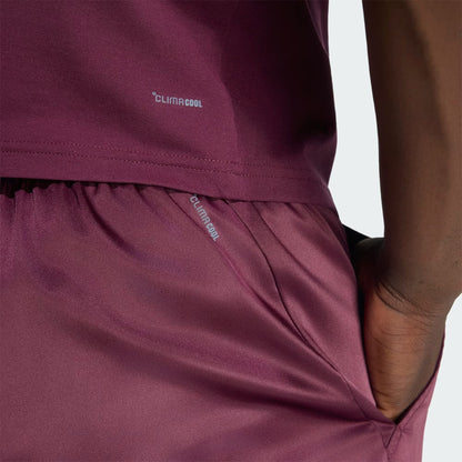 A person wearing a maroon adidas ClimaCool athletic outfit with their hand in their pocket, highlighting the shirt and the adidas Climacool Ergo Pro Men’s Tennis Shorts in maroon.