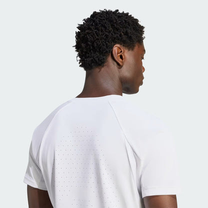 A person with short curly hair is shown from the back, wearing the adidas Climacool+ Freelift Pro Men’s Tennis T-Shirt in white, which features small perforations on the back, against a light gray background.