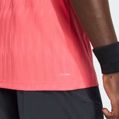 A close-up of a person wearing the adidas Climacool+ Airchill Freelift Men’s Tennis T-Shirt in Pure Turbo, paired with black shorts and a black wristband. The pink shirt from adidas features a subtle stripe pattern and incorporates Airchill technology for enhanced breathability, with “CLIMACOOL” visible near the hem.