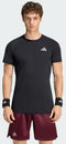 A man with curly hair wears an adidas Climacool+ Freelift Pro Men’s Tennis T-Shirt in black, maroon shorts, and black wristbands with white logos, standing facing forward against a plain light background.