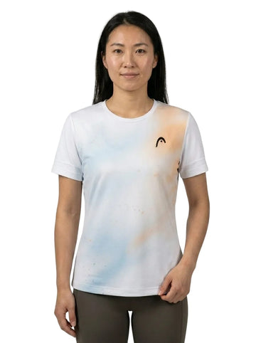 A woman with long black hair stands against a plain background wearing the HEAD Tie-Break II Women’s Tennis T-Shirt by HEAD—a white, breathable athletic shirt featuring light pastel blue and peach accents with a small black logo on the left chest.